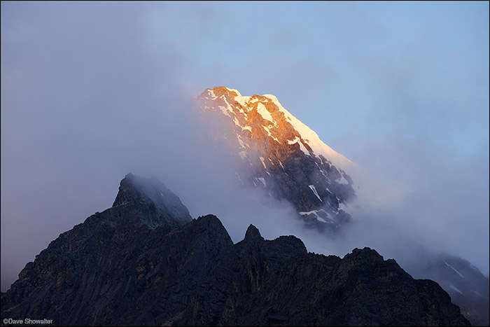 The very last light of the day breaks through heavy clouds to touch the summit of Auxilio (5560m) from our camp on the Huayhuash...