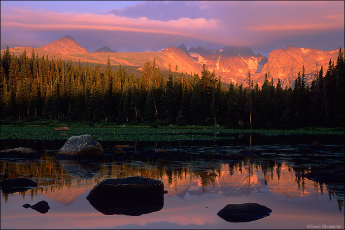 The jagged crest of the Indian Peaks in warm sunrise light, reflected in Red Rock Lake.&nbsp;