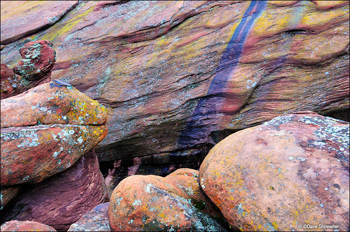 Colorful lichen-covered red boulders and a blue water track in a naturally arranged rock garden