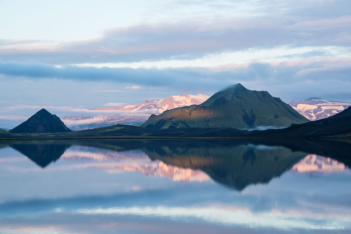Volcanoes are reflected in early morning light along the shore of Alfvatn, a beautiful lake on the Landmannalaugar Trek.&nbsp...