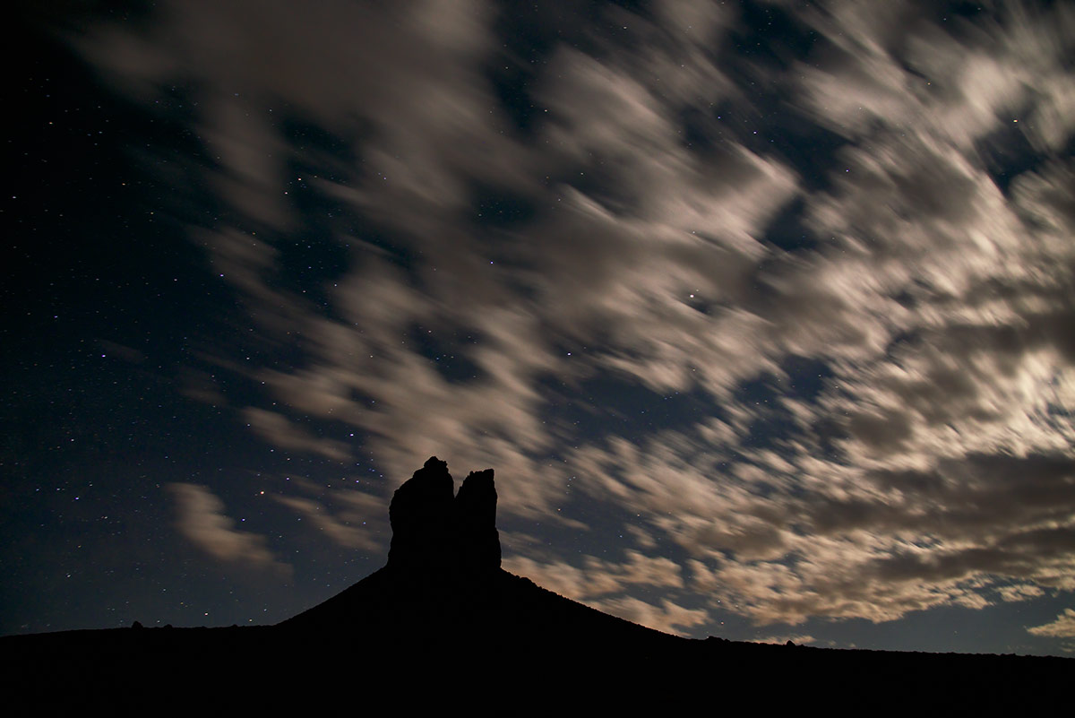 Clouds chased by winds aloft are lit by a bright half moon as night falls the week before summer solstice. The Boar's Tusk in...