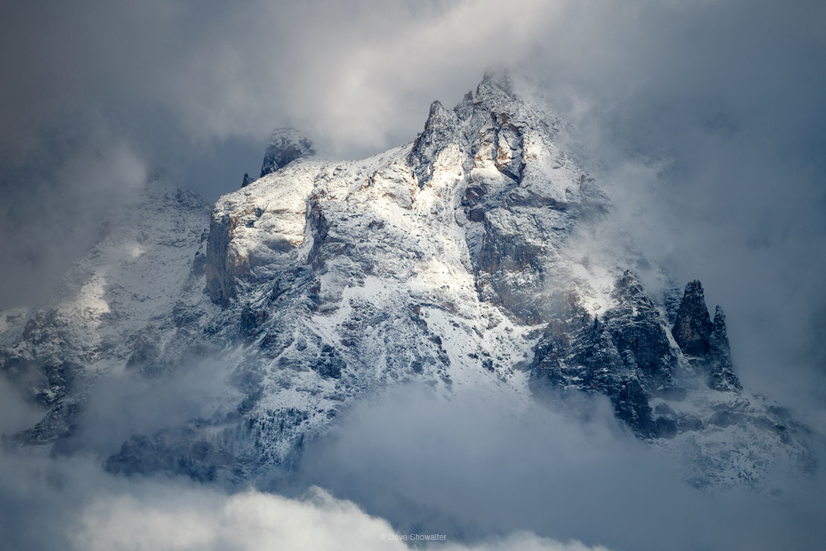 Like a curtain pulled back, a thick autumn cloud bank parts to reveal fresh snow on the Grand Teton in the Teton Range as a shaft...